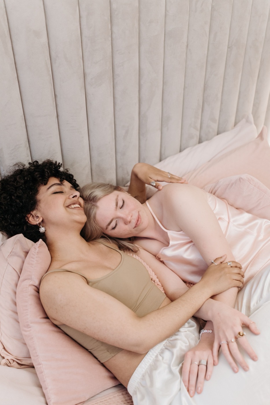 Two women cuddling peacefully in bed with soft pink pillows