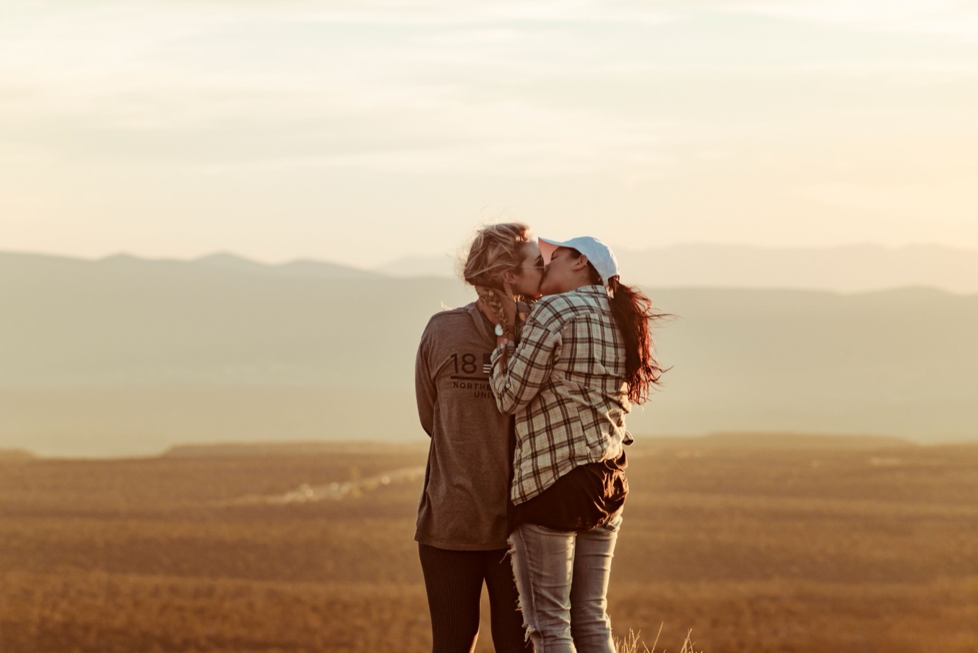 Two women kissing at a golden-hour overlook above a valley