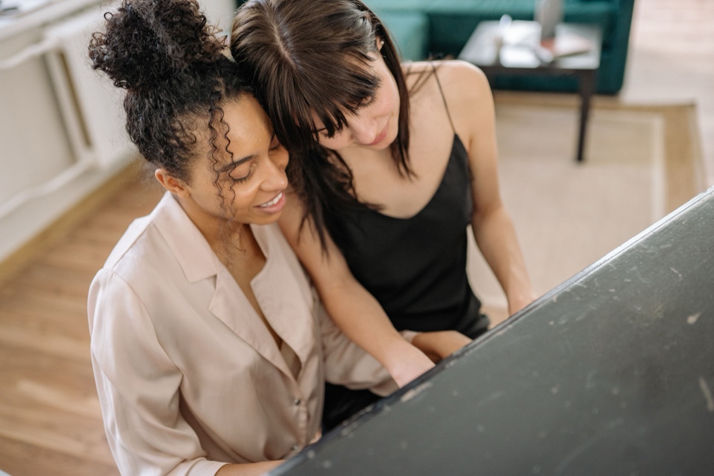 Two women sitting close at a piano looking at the keys together